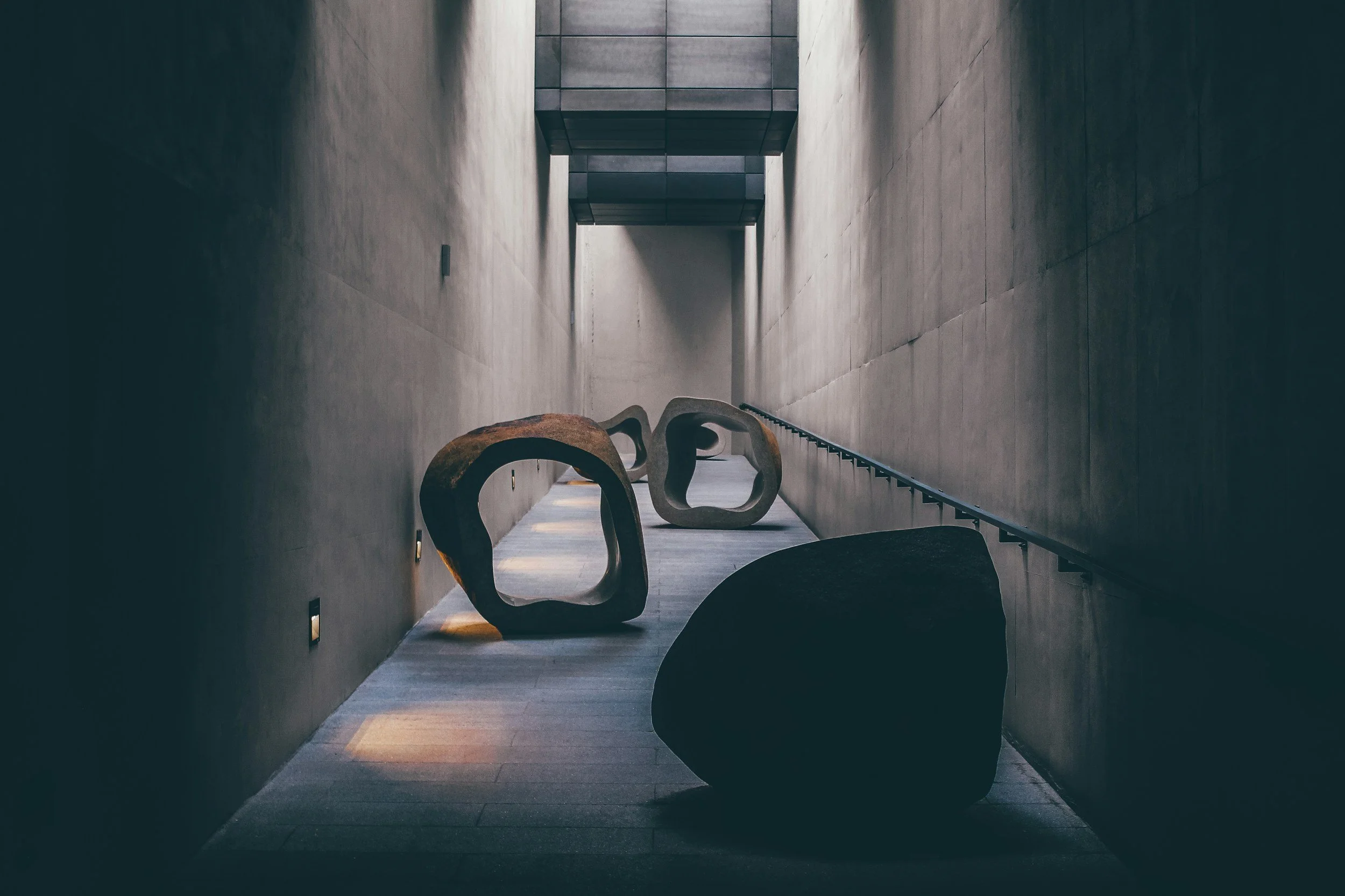 Minimalist hallway with three abstract wooden sculptures on the floor, concrete walls, and a modern design.